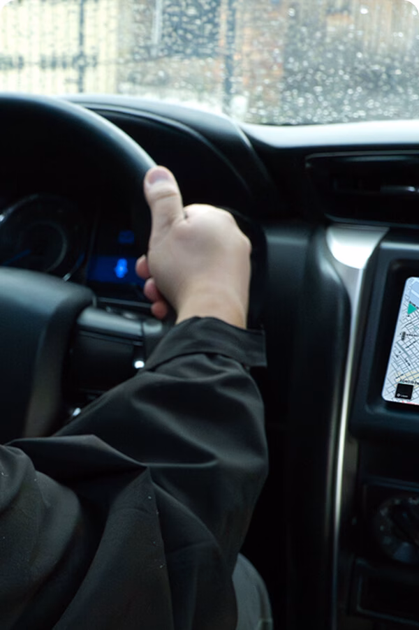 Hourly and full-day-img Hands on the wheel of a Toyota vehicle with GPS active, on a rainy day.