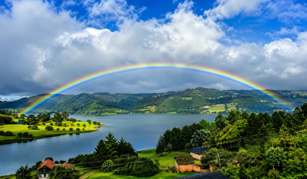 A rainbow over a green Andean reservoir surrounded by farmland