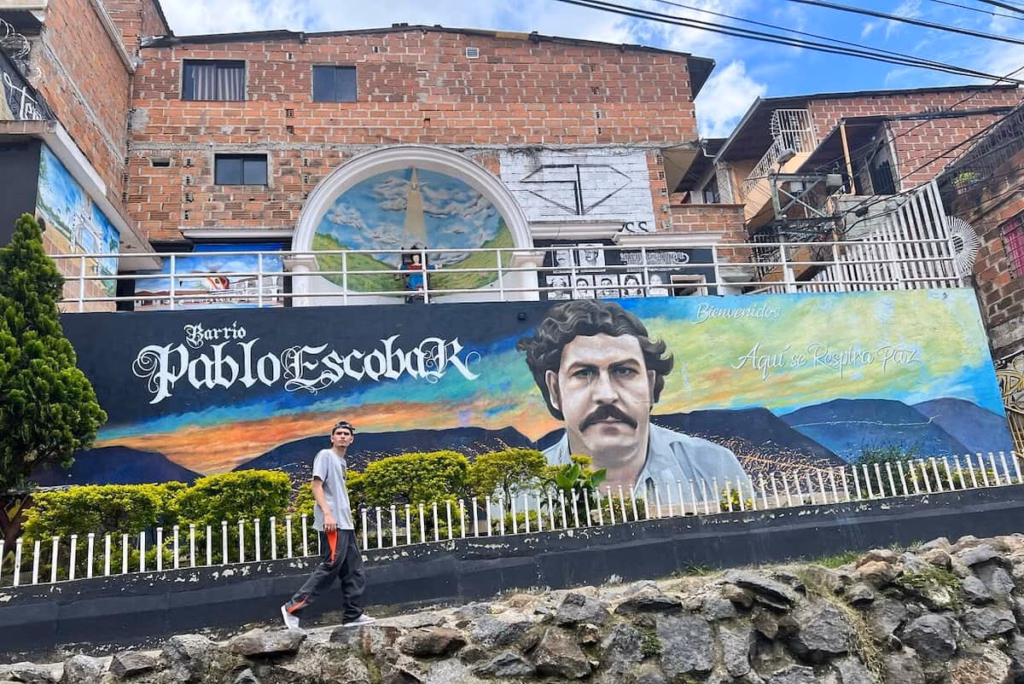 Mural callejero que dice Barrio Pablo Escobar con un retrato pintado y paisaje de montaña en Medellín