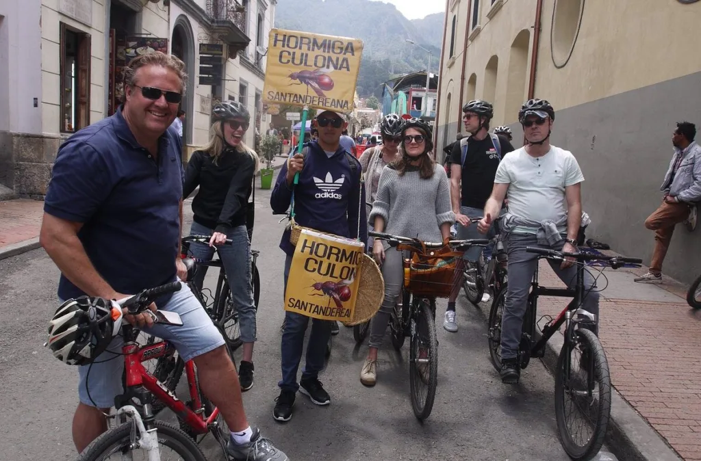 A rider holding a hormiga culona sign as the group stops in a narrow Bogota street