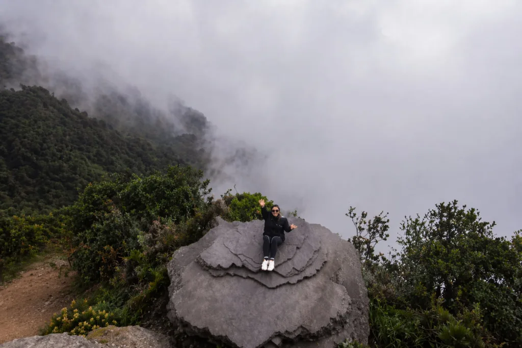 A visitor sitting on a rock viewpoint above the clouds at Chicaque