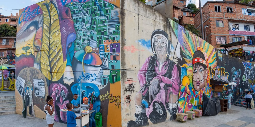 Mural of an older man in purple beside painted faces on a Comuna 13 walkway with residents passing