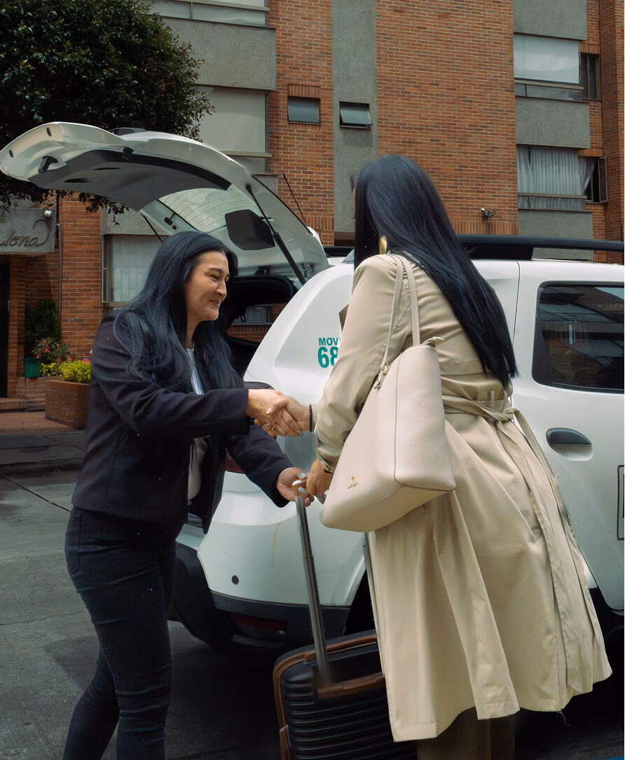 Female driver receiving a passenger's luggage next to a vehicle with the trunk open.
