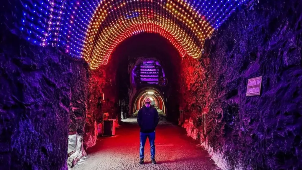 A visitor standing in a salt tunnel lit in red and purple at Zipaquira