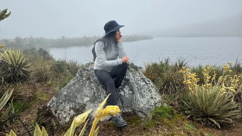 A hiker resting on a boulder beside a paramo lagoon in Sumapaz