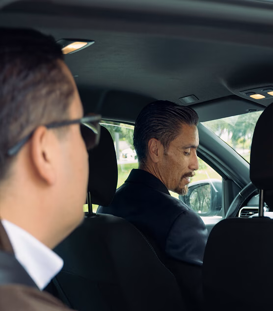 Two men talking in the back seat of a vehicle.