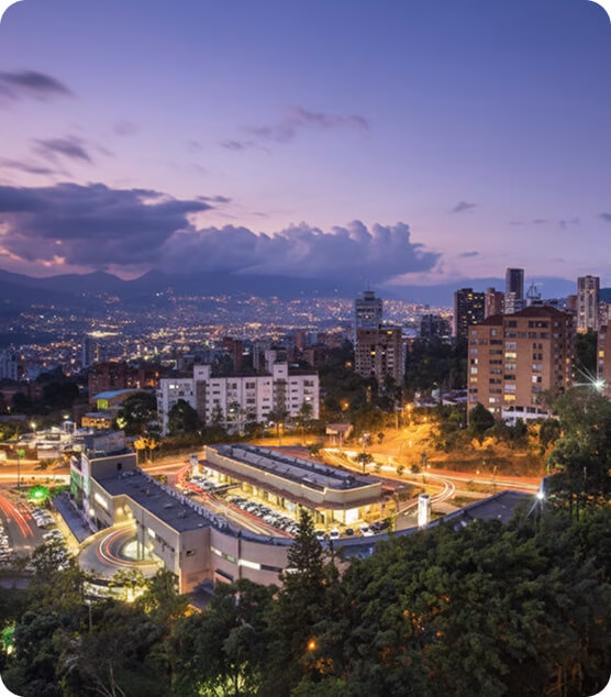 Panoramic view of MedellÃn at dusk, with illuminated buildings nestled among mountains.