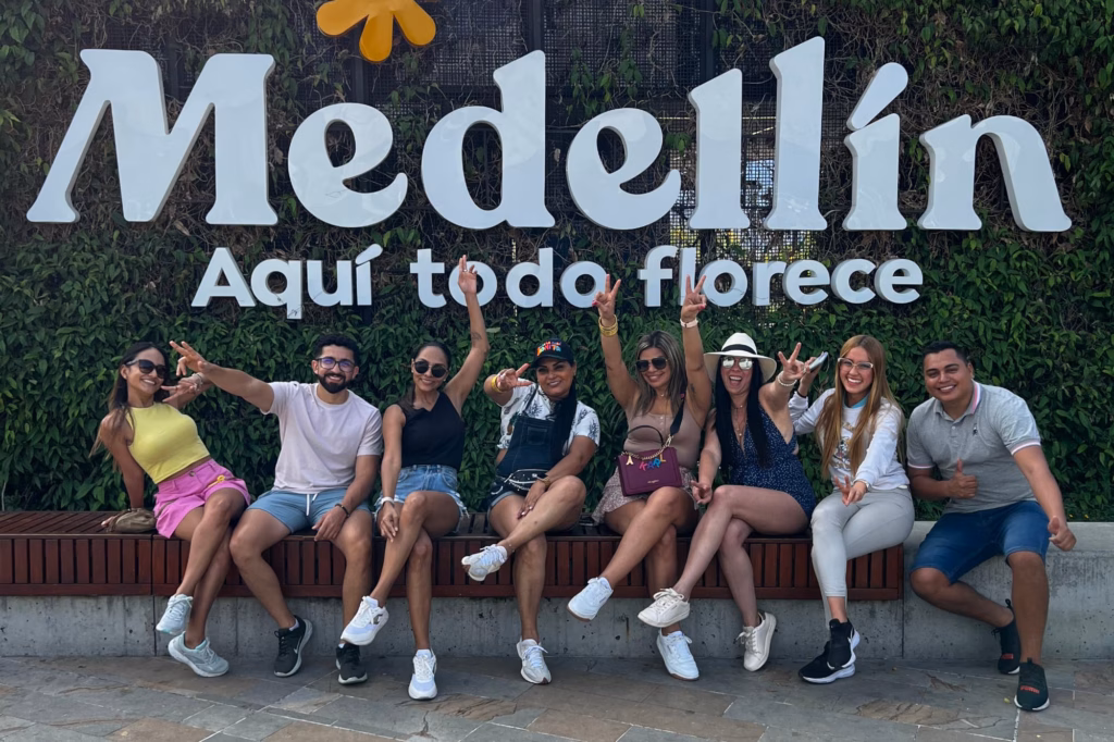 Viajeros sentados bajo el gran letrero Medellín Aquí todo florece