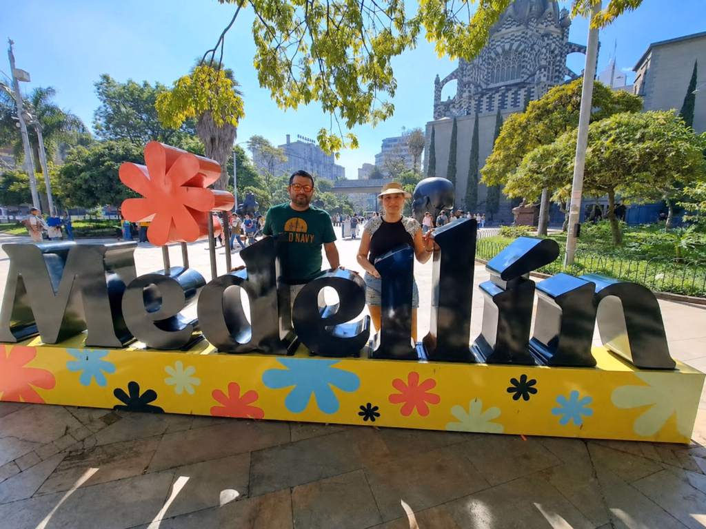 Two visitors beside the painted Medellín letter sculpture in a city park