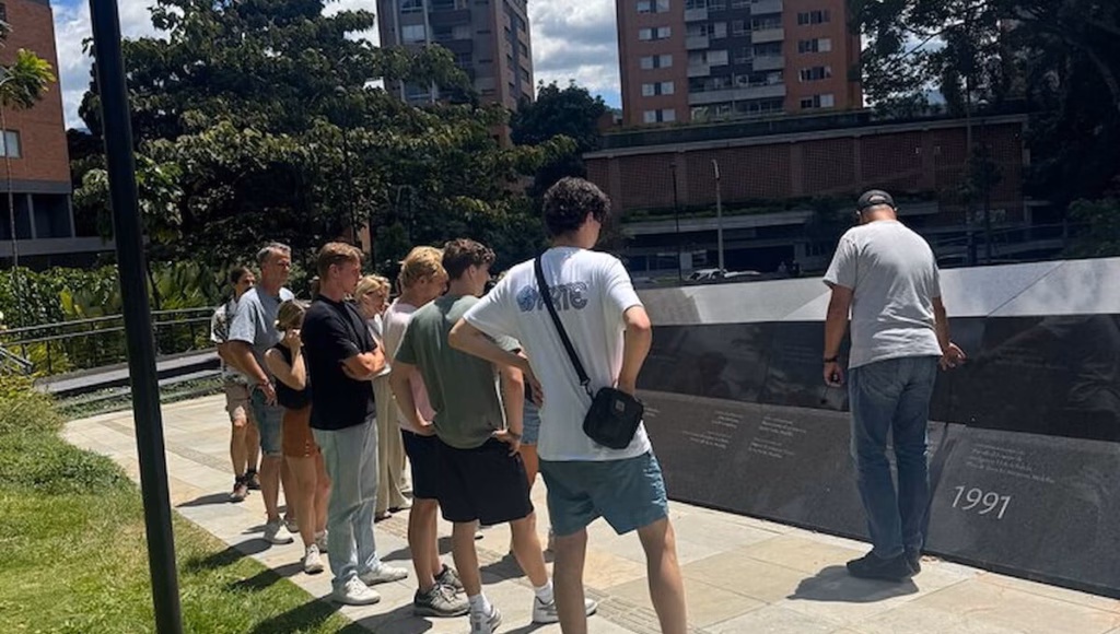 Visitors reading an engraved dark stone memorial wall on a guided Medellín tour